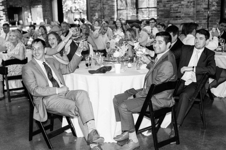 Wedding guests raising their glasses in a toast after a speech from the best man.