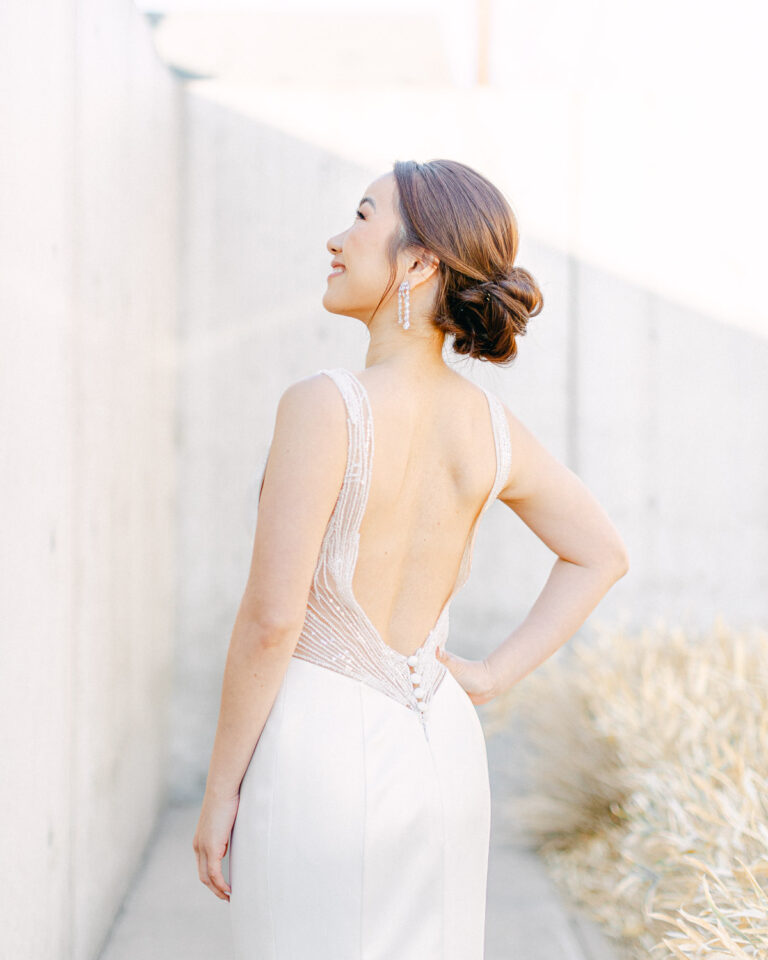 Bride standing during wedding portraits, wearing a backless wedding dress with delicate beaded straps.