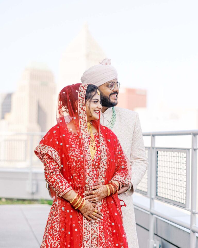 South Asian couple in vibrant traditional attire enjoying a moment on a rooftop with a view of Pittsburgh, PA, captured by James Tananan, wedding photographer and videographer.