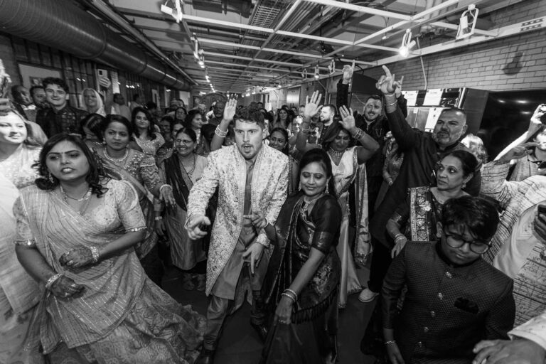 Groom's Baraat procession with excited guests joining him as he approaches the ceremony room, captured at a South Asian wedding by James Tananan, wedding photographer and videographer.