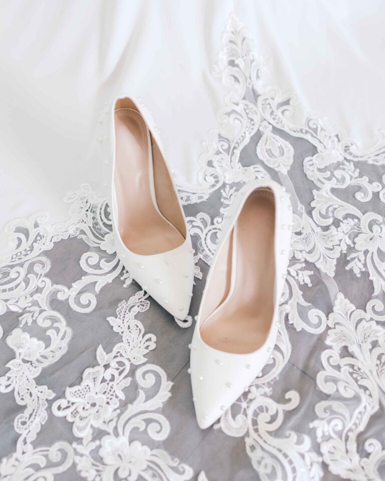 Ivory pointed-toe bridal heels placed on a white lace wedding dress.