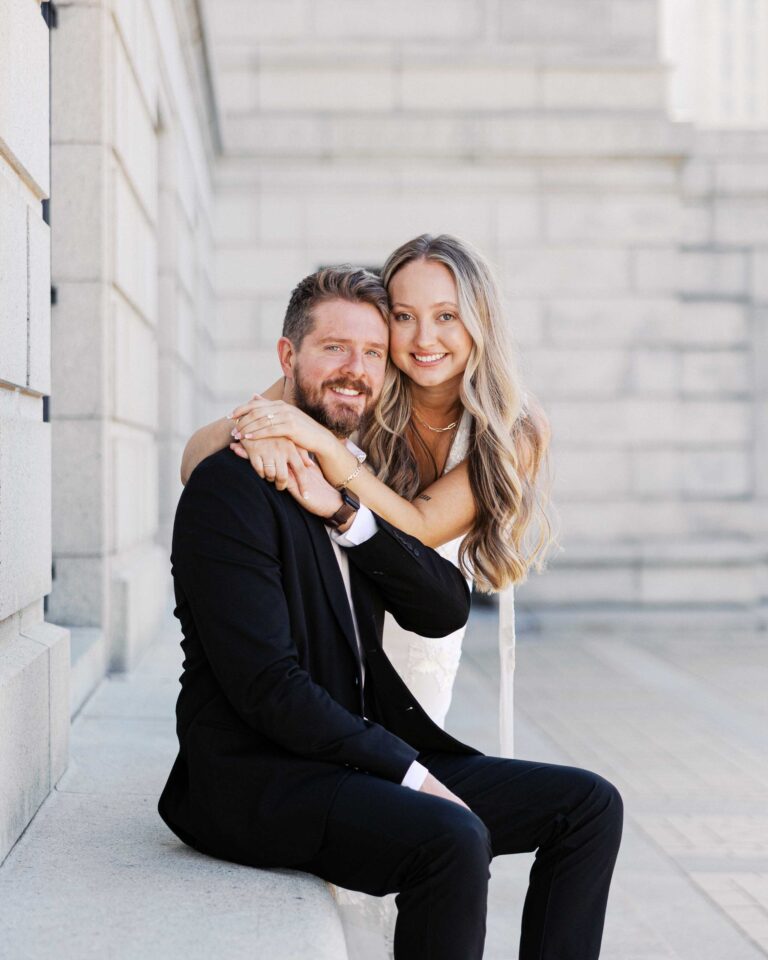 Engaged couple sitting together during an engagement session, smiling and embracing in soft natural light.