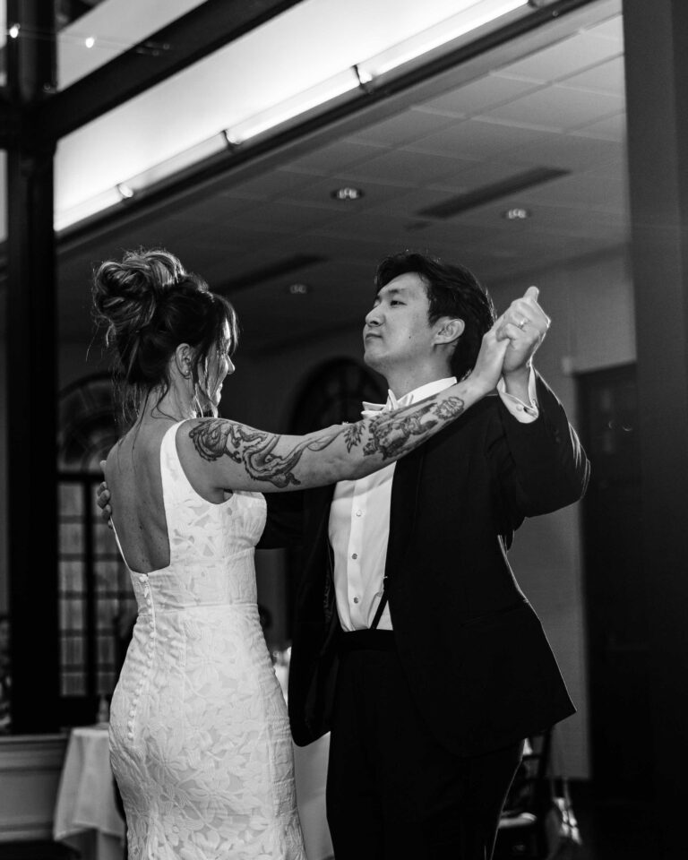 Bride and groom sharing their first dance during an indoor wedding reception, captured in black and white.