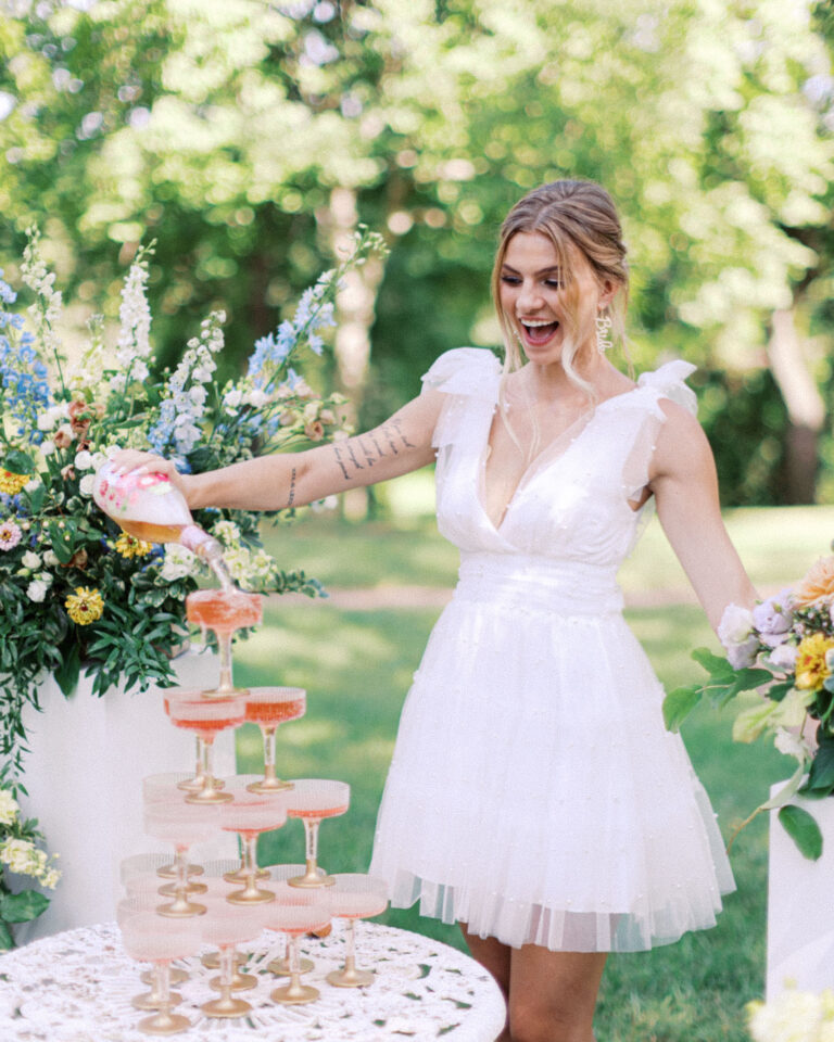 Bride pouring champagne into a coupe glass tower during a wedding celebration