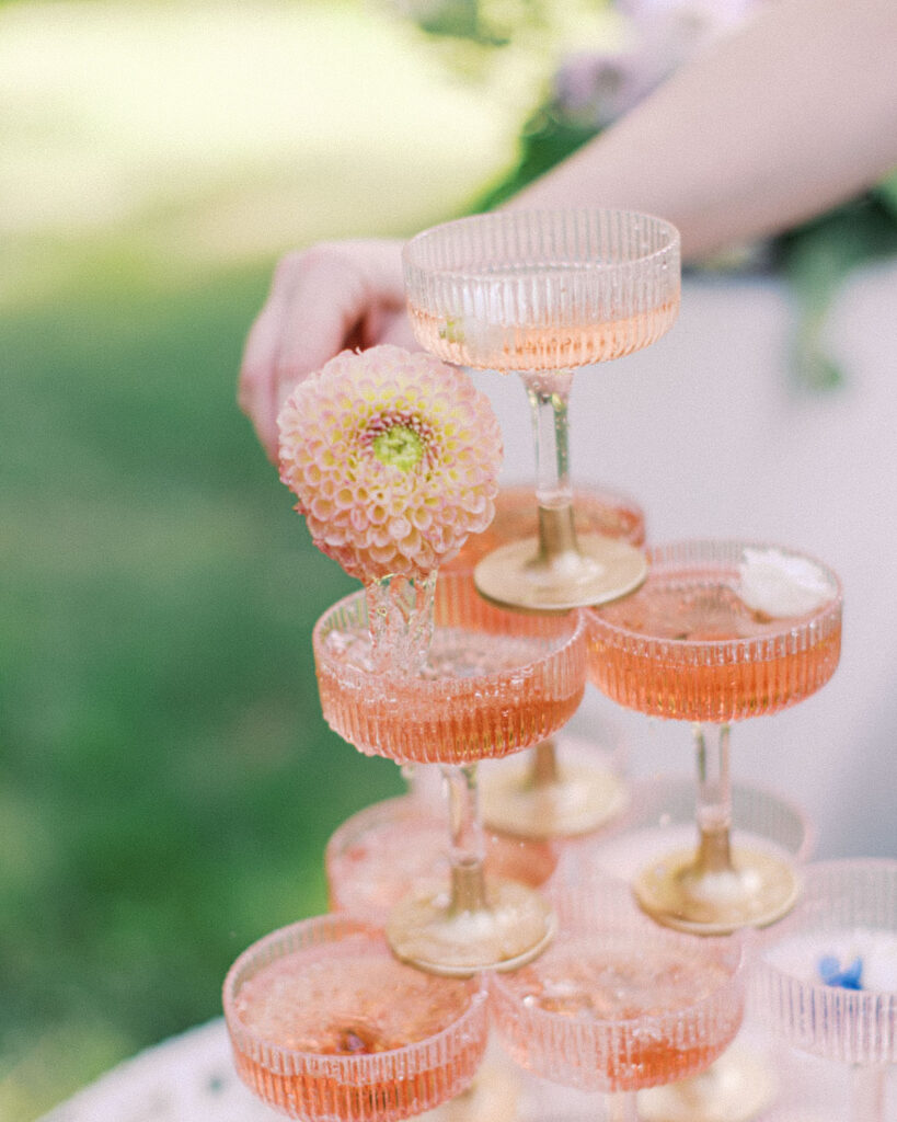 Hand placing a flower into a champagne tower made of coupe glasses