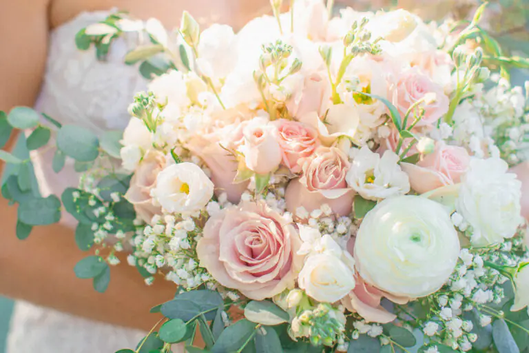 Soft blush and ivory wedding bouquet featuring roses, ranunculus, baby’s breath, and eucalyptus greenery.
